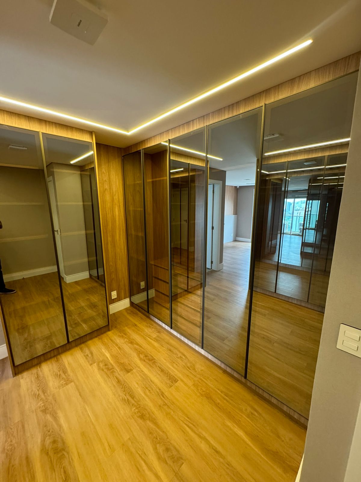 Closet amplo com portas espelhadas, iluminação em LED e marcenaria em madeira